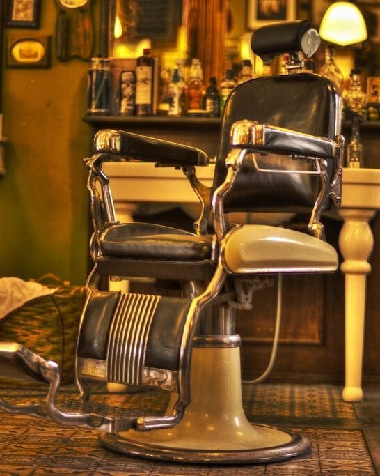 Silla de barbero clásica de cuero y cromo frente al mostrador, con luz cálida
