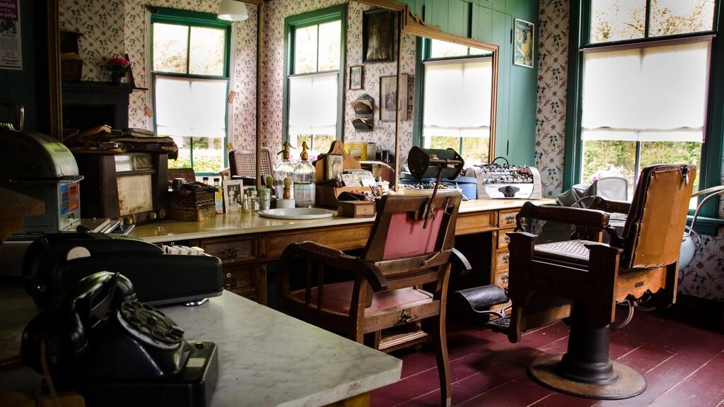 Interior de la barbería con sillas de madera y cuero, espejos grandes, piso vino y luz de ventana