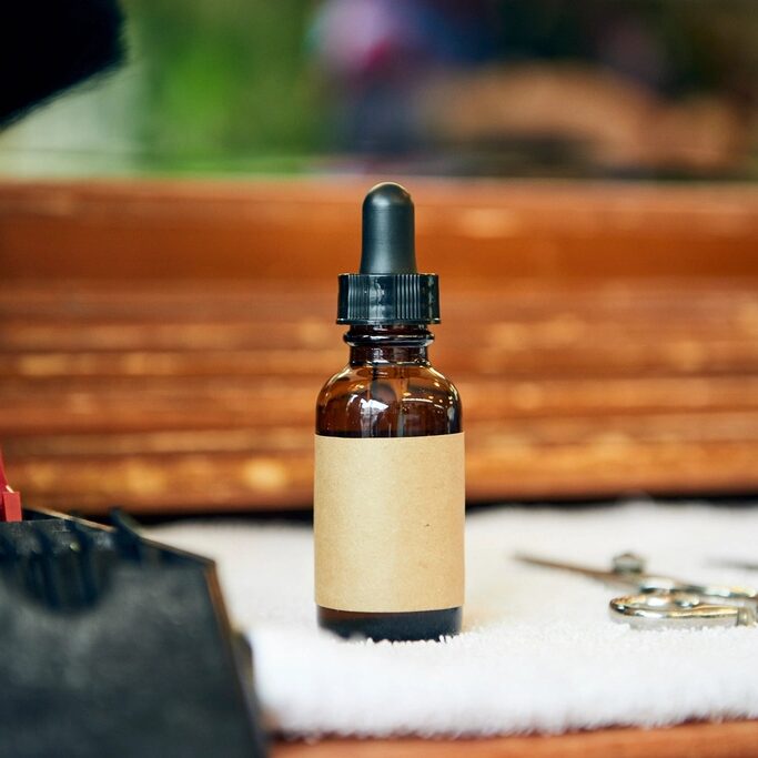 Frasco de aceite para barba sobre una toalla, junto a unas tijeras