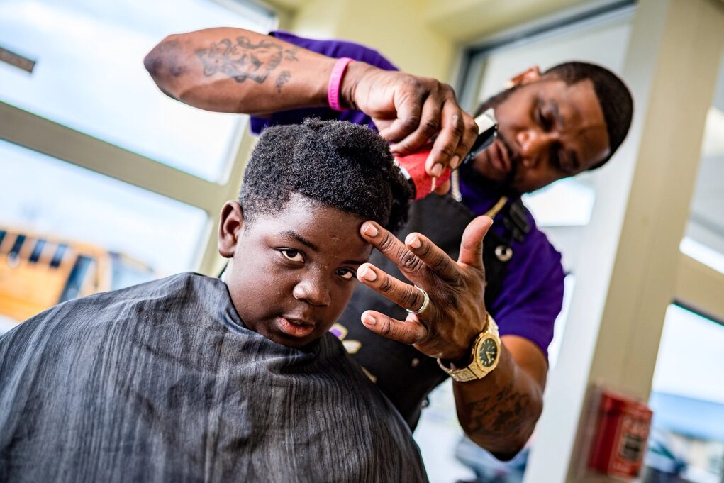 Niño con capa mirando a la cámara mientras el barbero le arregla el cabello