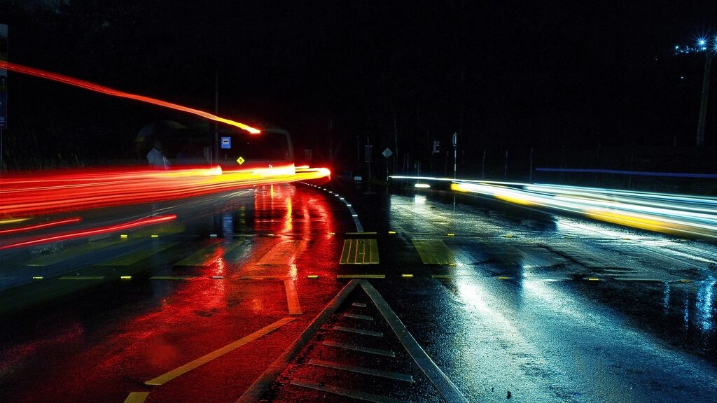Calle mojada de noche con luces rojas de los carros reflejadas en el asfalto