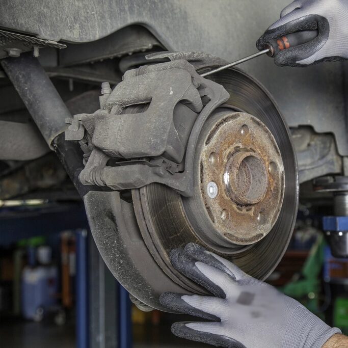 Manos con guantes revisando el disco y el caliper de freno de un carro subido en el elevador