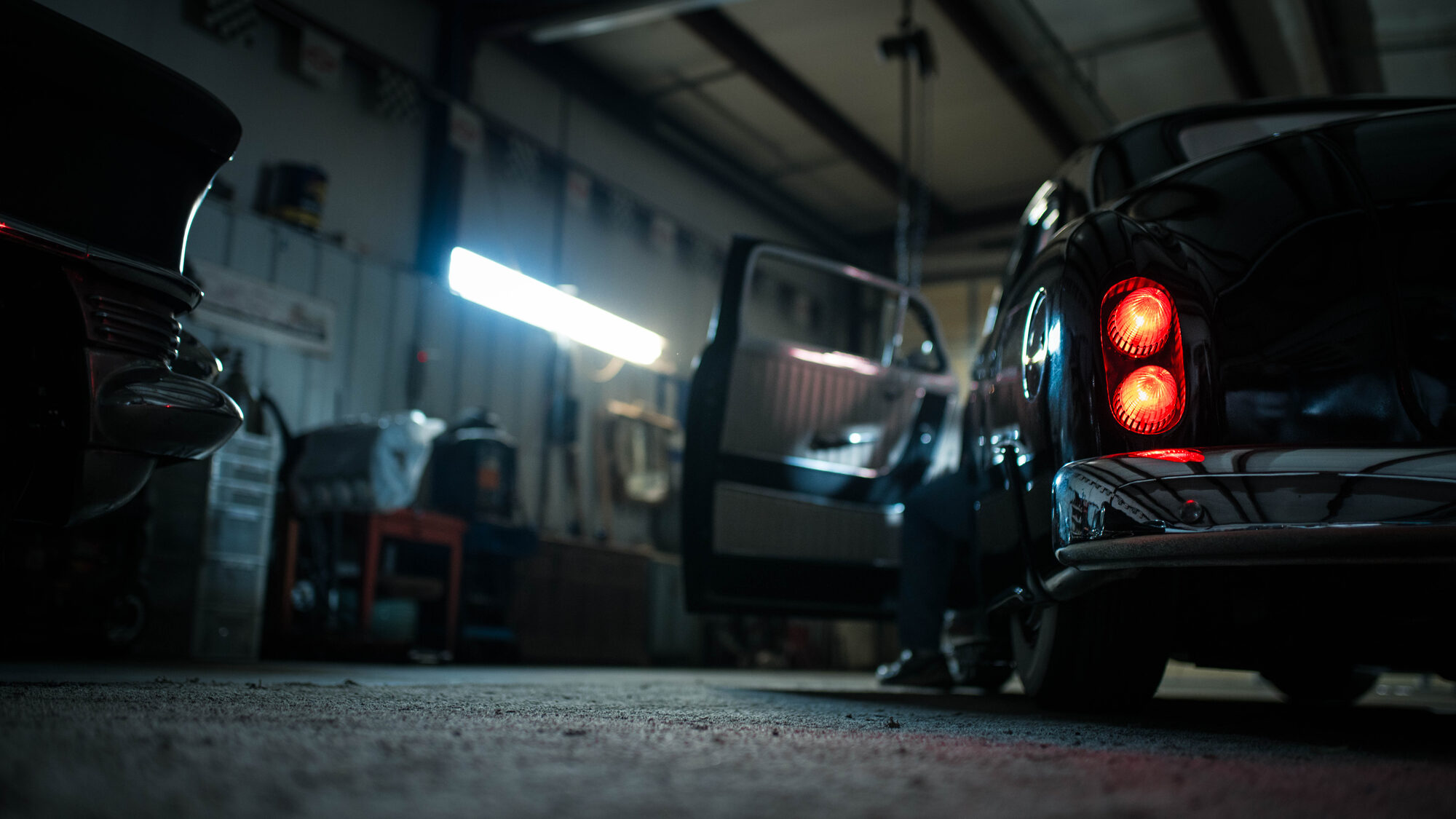 Garaje de noche con un carro negro de luces traseras encendidas y la puerta abierta junto a la lámpara de trabajo