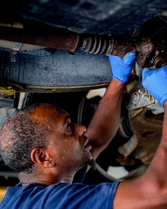 Mecánico con guantes trabajando debajo de un carro subido en el elevador